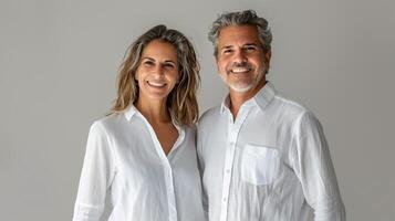 Smiling Middle-Aged Couple Holding Hands in White Shirts Against Neutral Background photo
