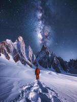 Stunning Night Sky Photo of the Milky Way Over Snow-Covered Mountains with Adventurer in Orange Gear