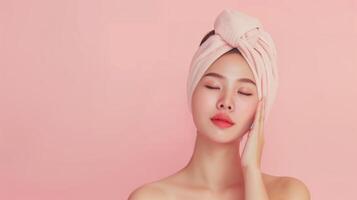 Serene Asian Woman with Towel on Head Embracing Skincare Routine on Soft Pink Background photo