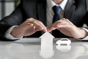 Businessman in Suit Protecting Paper House and Car with Hands Insurance and Financial Security Concepts photo