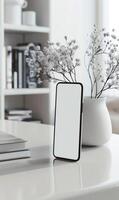 White Minimalist Smartphone Mockup on Desk with Modern Decor and Elegant Vase in Bright Workspace photo