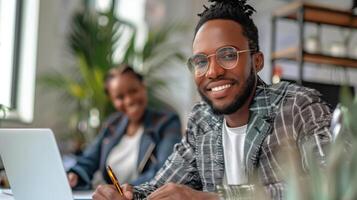 Smiling Professional Man Working in a Modern HR Office Environment with Laptop and Colleague in the Background photo