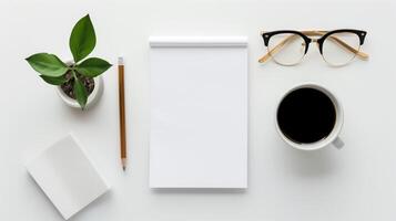 Top Down View of Minimal Workspace with Plant, Notepad, Pencil, Glasses, and Coffee Cup on White Background photo
