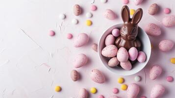 Easter composition - chocolate bunny, colored eggs and candies on pink stone background, top view photo