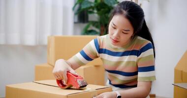 Selective focus, Young Asian woman wrapping cardboard boxes with duct tape in preparation for moving into new house. Moving house and lifestyle concept. photo