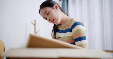 Selective focus, Young Asian woman is taking notes while checking belongings in cardboard boxes in preparation for moving to a new house. Moving house and lifestyle concept. photo