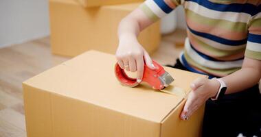 Selective focus, Hands of Young Asian woman wrapping cardboard boxes with duct tape in preparation for moving into new house. Moving house and lifestyle concept. photo