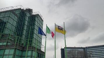 Italy, Milan 03. 2024 - The Italian flag, the European Union, and Agip flutters in the wind in slow motion against the background of office buildings and a cloudy sky and clouds video