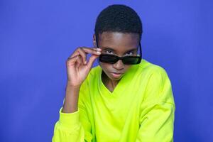 Fashion black model with sunglasses posing with attitude on blue studio background. photo