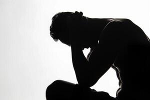 Silhouette of a man sitting with his head down on his hands, expressing suffering photo