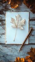 A white maple leaf placed on textured paper with an antique pen beside it on a rustic wooden surface during autumn photo