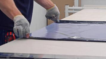 Workers in the production line are engaged in the process of pasting a sheet panel. They meticulously smooth it by hand and adhere it to a metal sheet. Slow motion. Close up. video