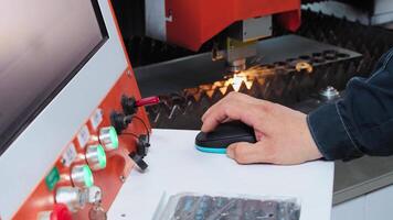 Close-up shot of an engineer's hand, as they use a computer to control and operate a laser-programmable metal cutting machine during production. Slow motion video