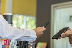 A woman uses an app on her smartphone to scan and pay for coffee at the coffee shop counter because it's convenient.Concept Scan to pay for goods with digital wallet or internet banking photo