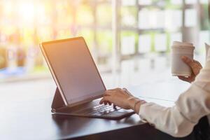 An Asian businesswoman holds a cup of coffee in her hand and drank while checking her computer online as she is starting a business that can order and check from anywhere online. photo