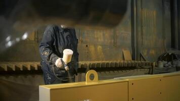 Worker in suit paints metal part with spray gun. Clip. Spray painting of large metal part at factory. Painting large metal objects or parts at factory video