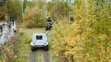 Walk on scooters along a narrow path. Clip.Green fields and forests around with quad bikes riding around during the autumn period. video
