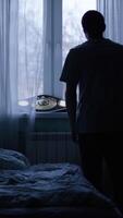 Alone man silhouette staring at the window closed with curtains in bedroom. Man stands at window alone video