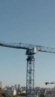 Top view of construction crane on background of city on sunny day. Stock footage. Construction cranes at height with view of city to horizon. Construction crane on background of modern city on sunny video