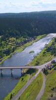 Aerial view of a picturesque valley with a village. Clip. Wide river crossed by a bridge and forested hills. video
