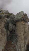 View near stone pillar of cliff. Shot. Top view of stone pillar of rock with approaching thick fog. Autumn landscape with colorful shrubs and dense gray fog on mountain video