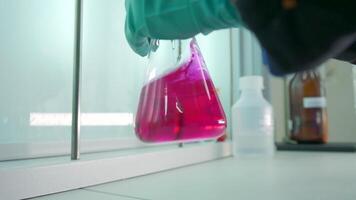 Close-up of flask with chemical liquid. Clip. Laboratory assistant conducts experiments with chemical liquid that changes colors. Chemical process in transparent flask in laboratory video