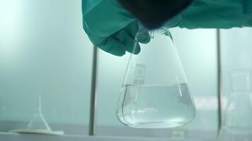 Close-up of flask with chemical liquid. Clip. Laboratory assistant conducts experiments with chemical liquid that changes colors. Chemical process in transparent flask in laboratory video