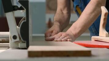 Close-up of man cutting board on machine. Creative. Carpenter processes wooden board on machine. Industrial processing and trimming of wooden boards with carpenters and machine tools video