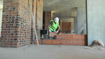 Bricklayer Working on Interior Wall Construction. A bricklayer, dressed in a high-visibility vest and hard hat, is seen working on an interior wall within a partially completed building. video