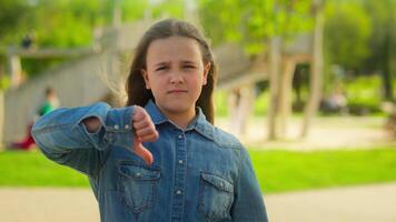 Sad upset displeased little girl schoolgirl child serious kid daughter in city outdoors looking camera showing thumb down finger gesture dislike not low mark disapprove sign childhood custody problem video