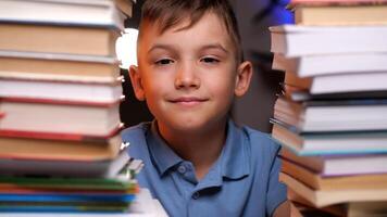 Smart boy smiling and sitting behind a big stack of books photo
