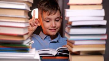 Smart schoolboy having an idea while reading a book surrounded by books photo