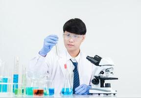 Man asian student education learning scientist wearing doctor gown in lab looking hand at chemist. caused by mixing reagents in scientific research laboratories with test tubes and microscope on table photo