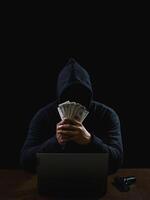 Portrait hacker spy man one person in black hoodie sitting on table looking computer laptop used login password attack security to data digital internet network system night dark background copy space photo