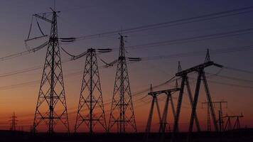 Silhouette of high-voltage poles against the background of the sunset sky. Power tower. Distribution of high voltage current along the power line. Electrical substation video