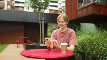 Smiling Caucasian Woman Using Smartphone and Surfing the Internet while Holding a Takeaway Latte Coffee Cup in cafe. video