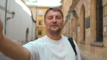 Handsome man taking selfie with smart mobile phone device or call by camera on city street. Happy tourist visiting Krakow old town. video