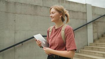 Side view of adorable Caucasian woman holding tablet laptop device while browsing Internet. Searching necessary information. Standing before modern building on street. video