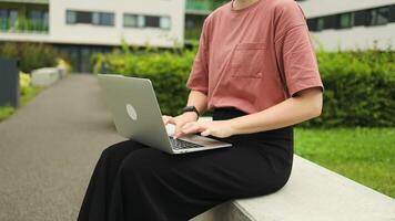 Caucasian woman in at-shirt working on a laptop at city centre Female student on campus sitting on a bench. video