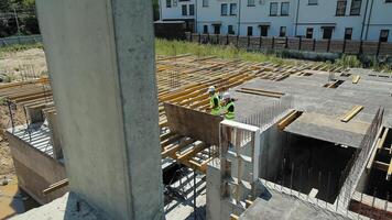 Aerial View of Construction Workers at Building Site. Aerial view captures two construction workers in high-visibility vests as they maneuver a large wooden board across a building site. video