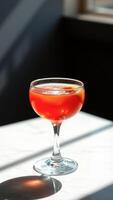 Red Cocktail with Ice and Orange Slice in a Glass on White Marble photo