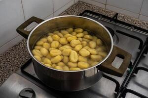 A pan of gnocchi simmering over a flame on a stovetop in a traditional restaurant kitchen, with golden pieces gently cooking in the rustic setting. photo