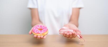 woman hand hold Donut with tape measure, choose stop eating sweet is Unhealthy ealthy food. Dieting control, Weight loss, Obesity, eating lifestyle and nutrition concepts photo