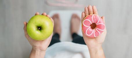 woman on weight scale and hand hold green Apple and donut, choose between fruit is Healthy and sweet is Unhealthy junk food. Dieting control, Weight loss, Obesity, eating lifestyle and nutrition photo