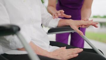 Physiotherapist helping elderly woman patient stretching arm during exercise correct in hand during training hand with patient Back problems in the garden. Caregiver, old woman and nurse in park. video