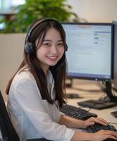 Smiling Chinese female customer service staff wearing headphones and working at office desk photo