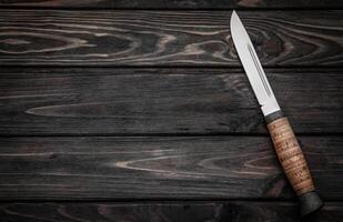 Hunting bowie knife with a wooden handle on dark wooden background. Steel arms weapon. top view photo