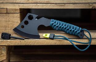 A small black ax with a paracord-wrapped handle. A tool for cutting branches or firewood in the forest. Self defense weapon. Wooden back. photo
