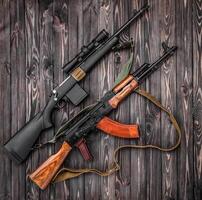 Two weapons lie on a plank surface. An old Soviet automatic carbine and a modern bolt-action rifle with a telescopic sight. Weapon on a wooden back photo