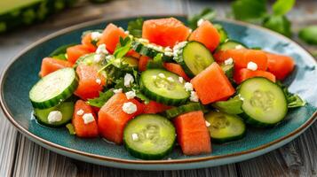 Cucumber salad with thinly sliced cucumbers watermelon cubes and feta cheese crumbles on a turquoise ceramic plate with a rustic wooden background photo